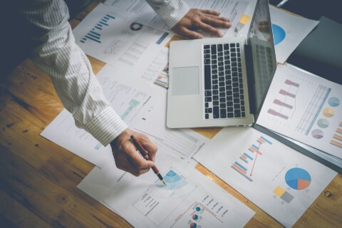 Business professional analyzing financial and project data charts on desk with laptop, illustrating SaaS growth and strategy planning.