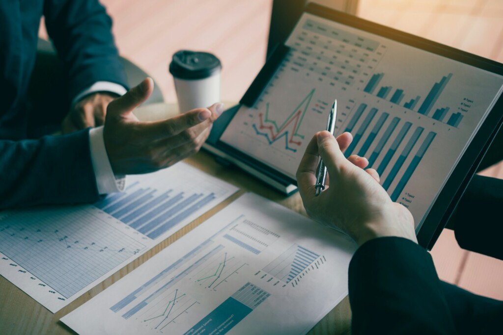 Business professionals discussing financial graphs and data analytics displayed on tablet and printed sheets, illustrating strategic planning and performance analysis.