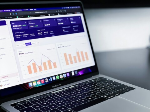 Close-up of a MacBook Pro displaying a SaaS analytics dashboard with revenue, subscription, sales, and growth rate charts