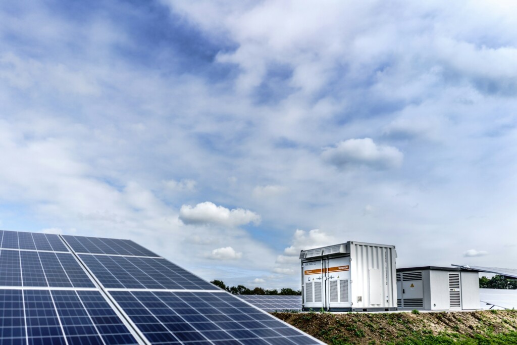 Solar panels with a large battery energy storage unit under partly cloudy sky, illustrating clean renewable energy storage technology