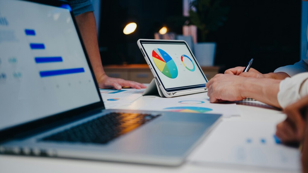 Business team analyzing SaaS data on laptop and tablet dashboards with colorful charts and graphs in a modern workspace.
