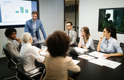 Diverse group of professionals in a tech startup meeting discussing AI regulation and business growth strategies, with charts and laptops visible on the table.
