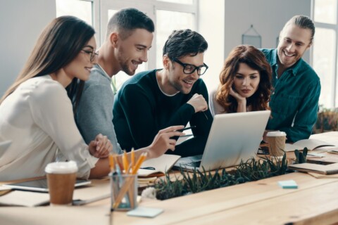Diverse startup team collaborating and brainstorming around a laptop in a modern office, highlighting trust, transparency, and innovation in a business ecosystem.